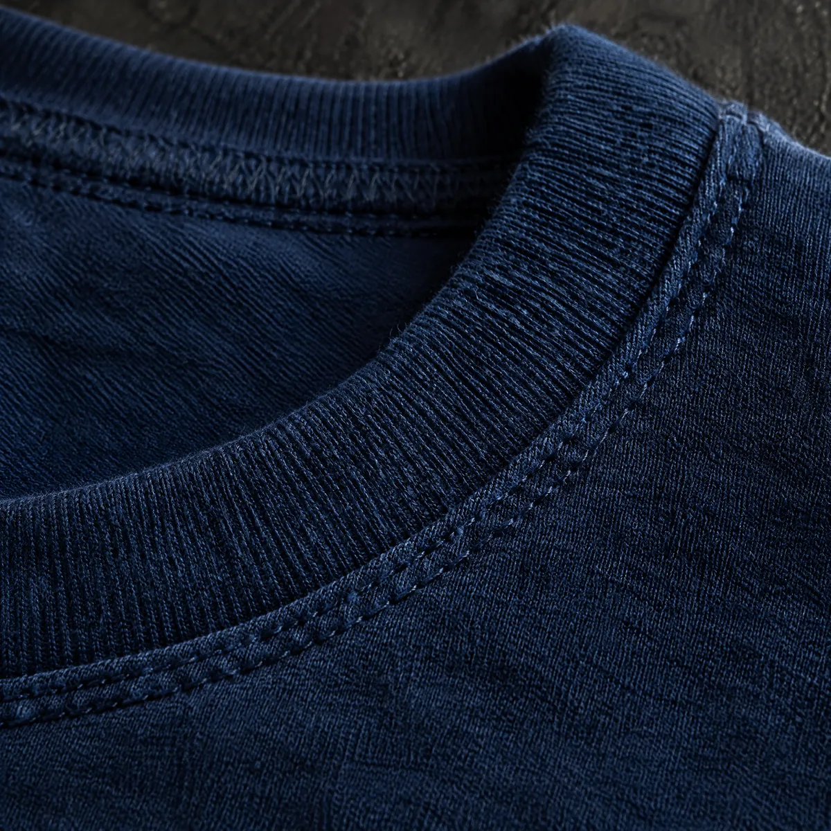 Macro view of a coverstitched rib neckline on indigo jersey.
